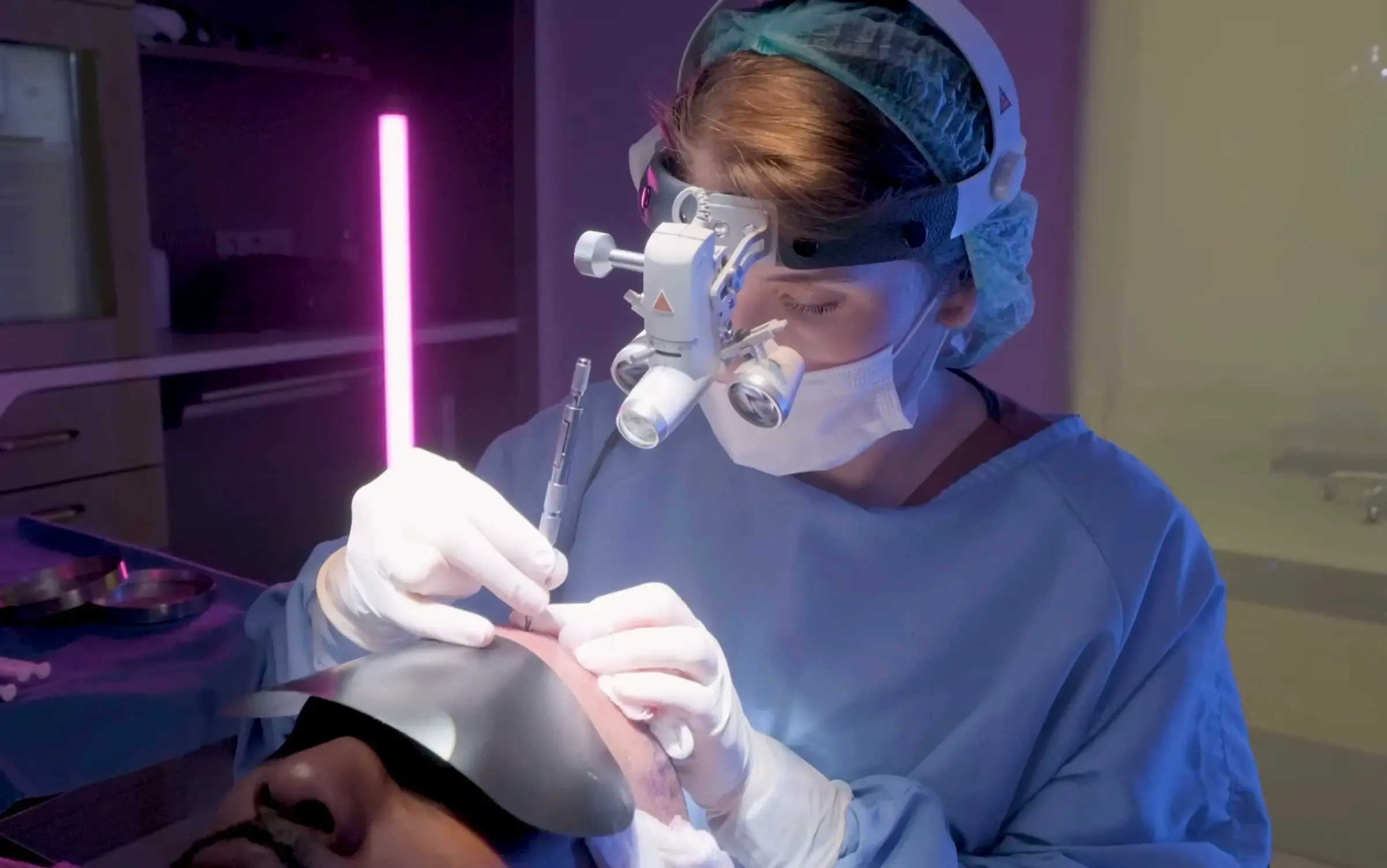 A Vera Clinic surgeon in a mask and surgical loupes implanting grafts under the operating light