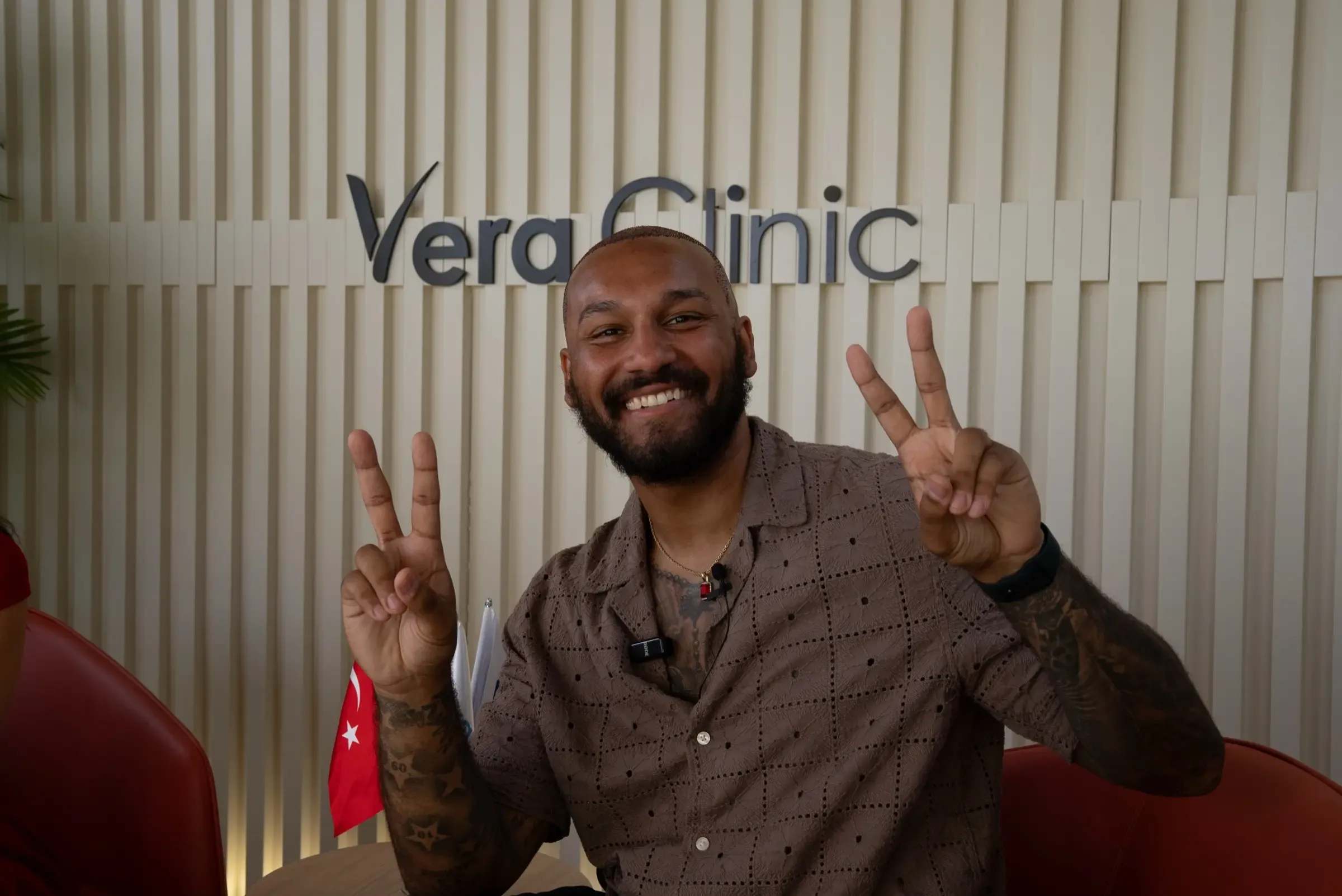 A smiling patient raising both hands in a victory sign in front of the Vera Clinic sign