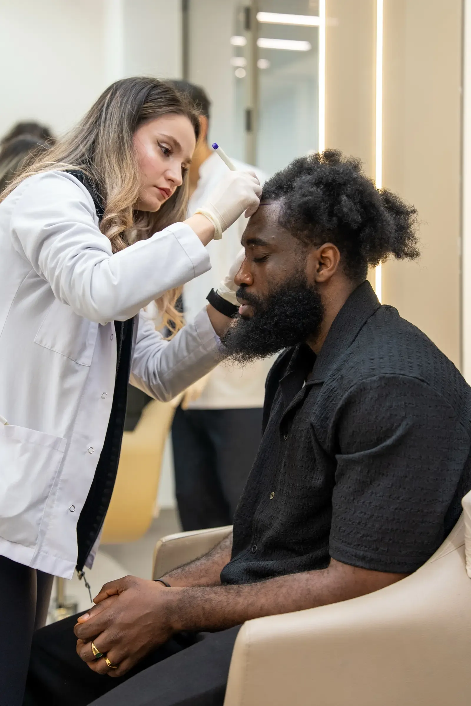 A Vera Clinic clinician marking the front hairline of a seated patient with afro-textured hair